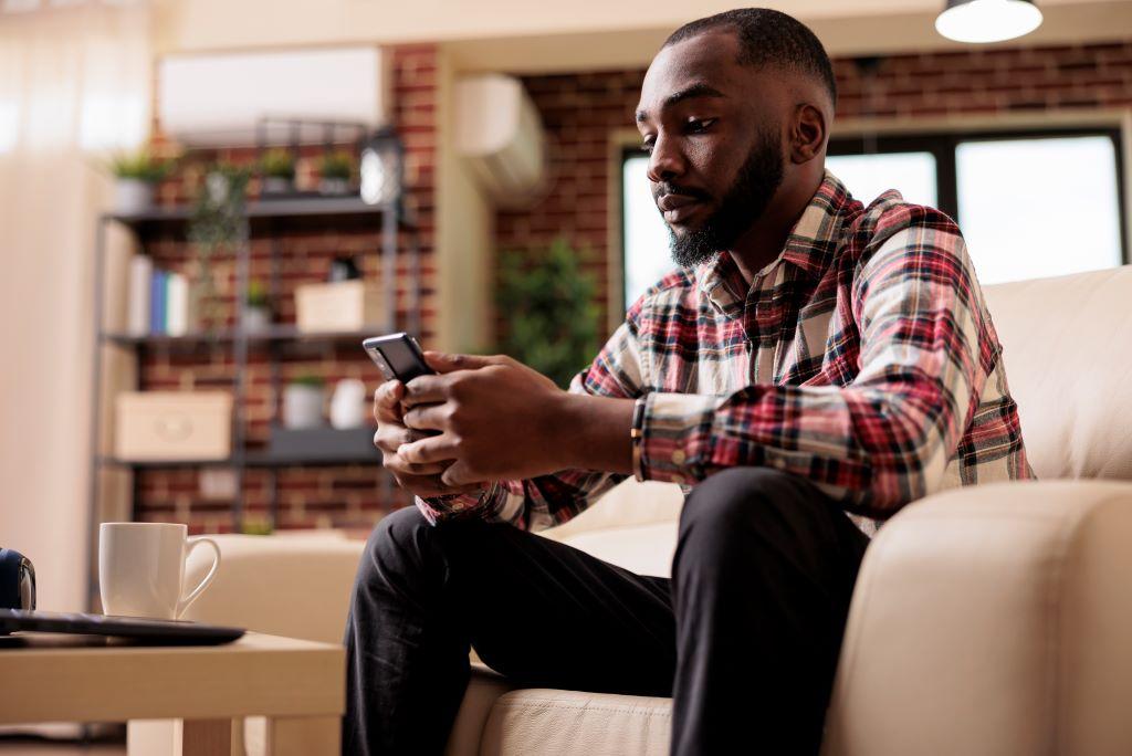 a man sitting on a sofa is checking something on his mobile phone